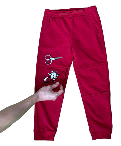 Pair of deep red Chakiboo™ RenewaKnee™ durable double-knee kids' pants with scissors on the left leg and a hand peeling off the snipped outer knee layer
