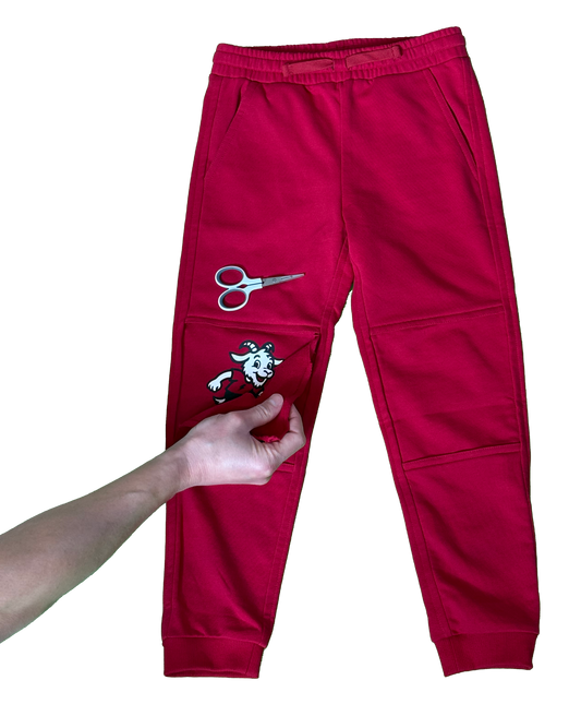 Red sweatpants with a cartoon goat on a skateboard.  Scissors above the knee to indicate cutting a stitch so as to remove the extra knee layer.  Hand peeling off the extra layer.